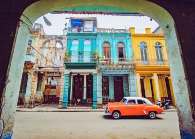 Orange and white sedan parked beside brown concrete building during daytime, Havana, Cuba